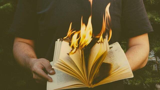 Un hombre sostiene un libro ardiendo.