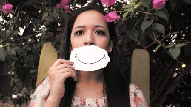 Chica disimula su tristeza con una sonrisa de papel delante de la boca.