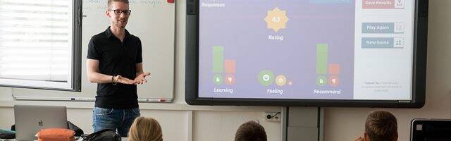 Profesor dando clase a niños con una pantalla.