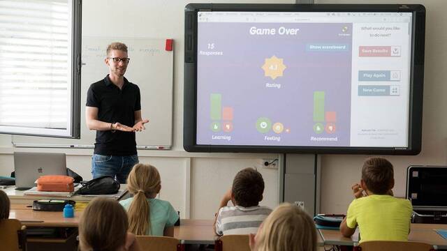 Profesor dando clase a niños con una pantalla.