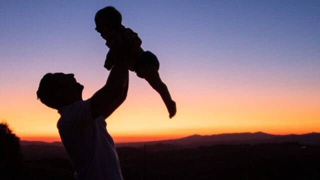 Hombre sostiene en el aire a su hijo.