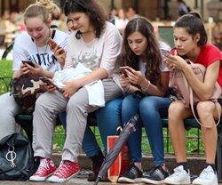 Cuatro chicas sentadas en un banco mirando el teléfono móvil.