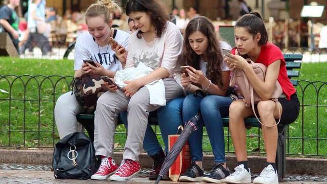 Cuatro chicas sentadas en un banco mirando el teléfono móvil.