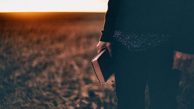 Una mujer en el campo, en el ocaso, con una Biblia.