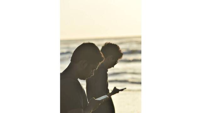 Dos hombres en la playa mirando el móvil.