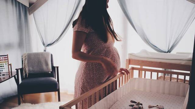 Mujer embarazada contempla la cuna vacía que espera a su bebé.