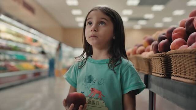 Una niña con un melocotón en la mano mira a su madre en el supermercado.