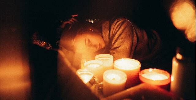 Una mujer joven con velas, quizá orando, en una foto de Harvey Robinson para Unsplash