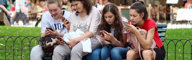 Cuatro adolescentes sentadas en un parque mirando su móvil.