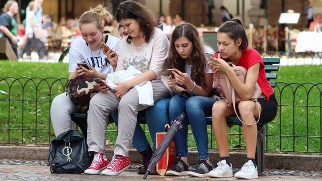 Cuatro adolescentes sentadas en un parque mirando su móvil.