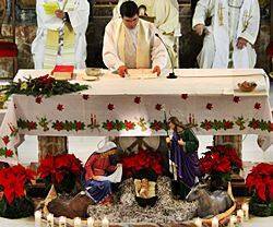 Un sacerdote celebra la Misa del Gallo con un belén delante del altar.