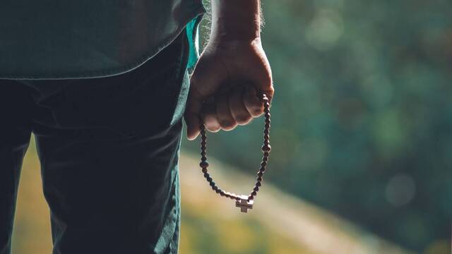 Joven de espaldas sosteniendo un rosario.