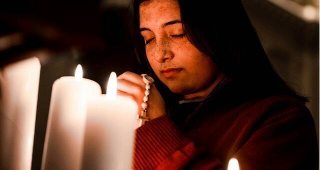 Una joven reza con velas y el rosario, foto de Gianna B para Unsplash