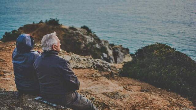 Un anciano matrimonio contempla el mar, sentados.