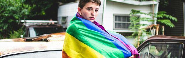 Adolescente de sexo indefinido envuelto en la bandera arco iris.