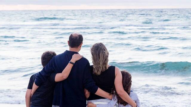 Una familia contempla abrazada el mar.