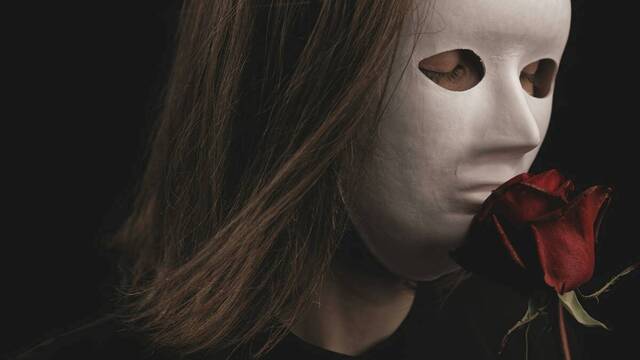 Una mujer con máscara blanca huele una rosa.