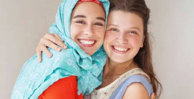 Dos chicas jóvenes se abrazan sonrientes, una de ellas con la cabeza cubierta con un velo musulmán.