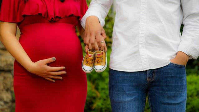 Una pareja, con ella embarazada, sostiene las zapatillas del futuro bebé.
