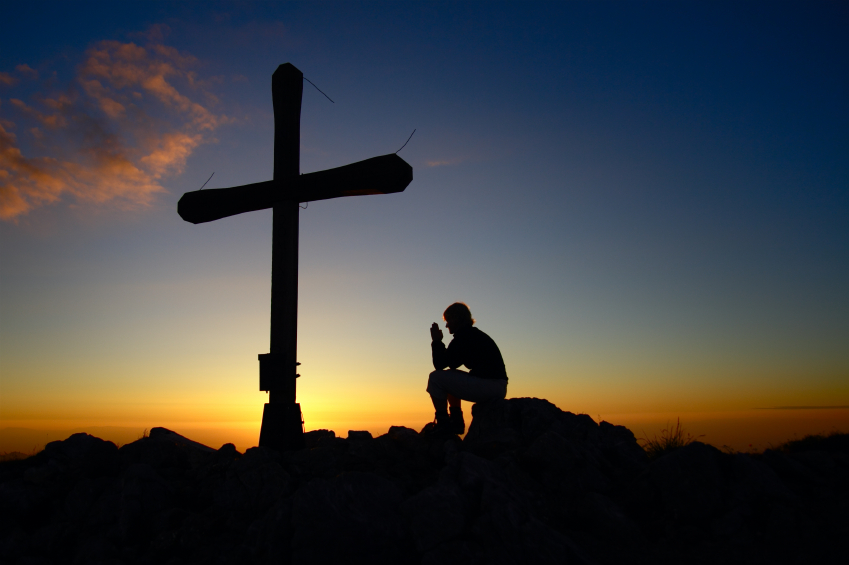 Un hombre reza al atardecer ante una cruz.