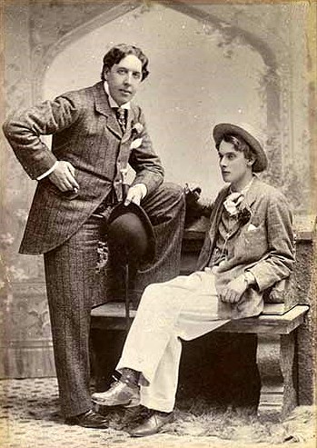 Oscar Wilde, de pie, junto a Lord Alfred Douglas, sentado.